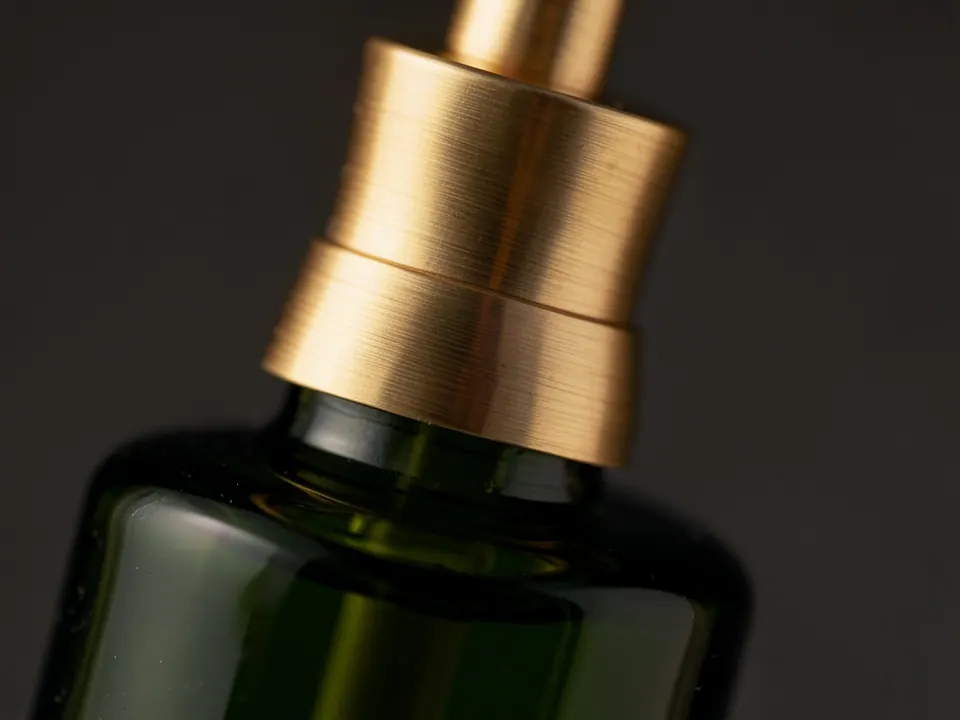 Macro photograph of a brushed brass pump on a dark green bottle